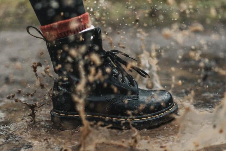 black boot stepping into a brown mud puddle
